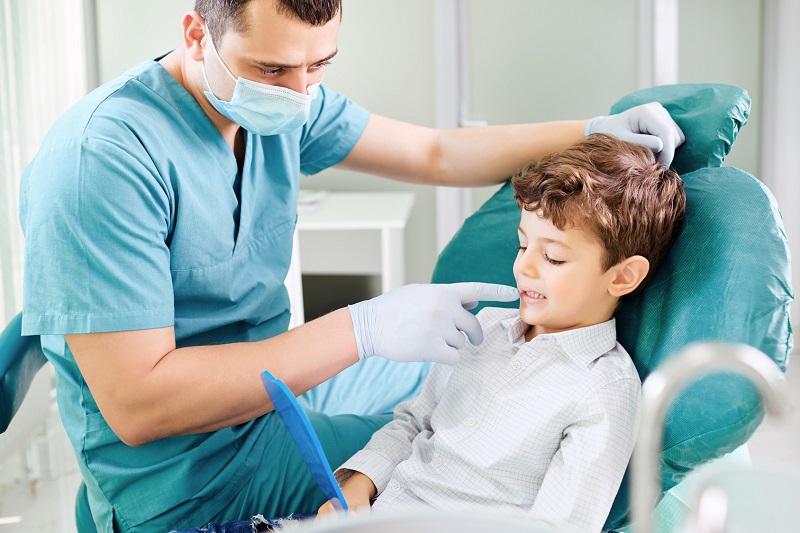 Boy child and dentist are checking teeth in the mirror.